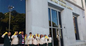  Trabalhadores da limpeza erguem as mãos vestidas com luvas amarelas na Avenida Paulista